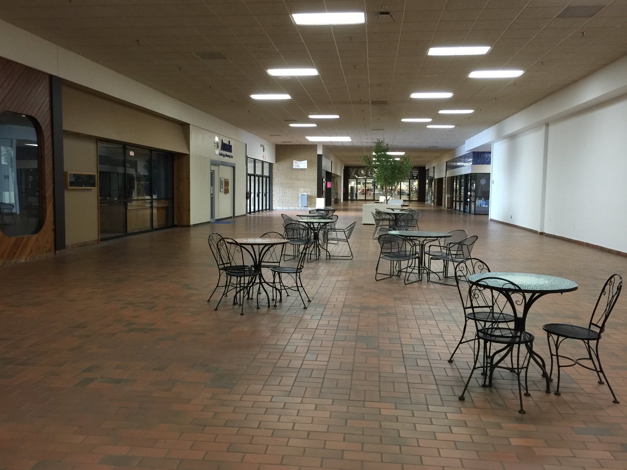 A liminal empty mall with empty tables and chairs in a long empty walkway.