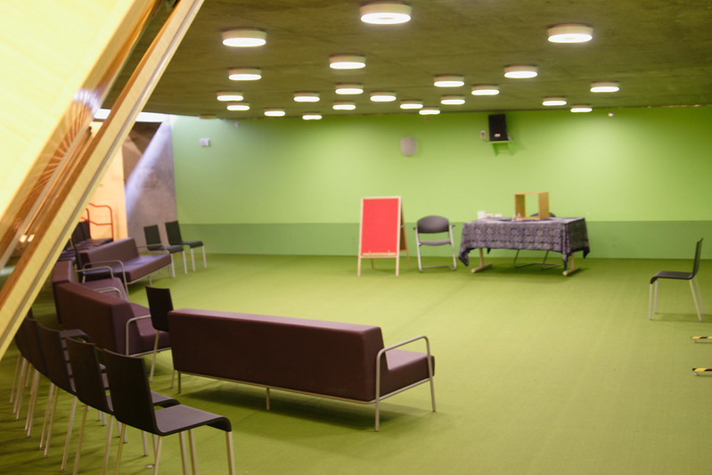 An empty green room that looks like a backroom with purple chairs.