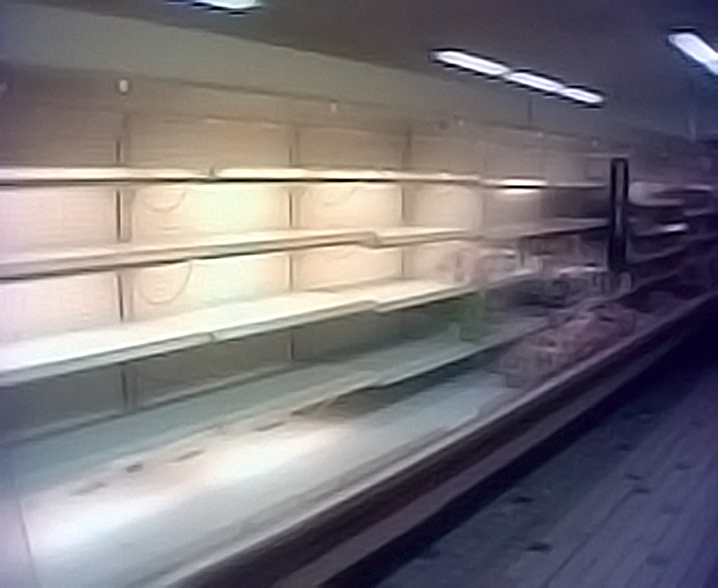 A blurry vhs style photograph of empty shelves in a supermarket at night.